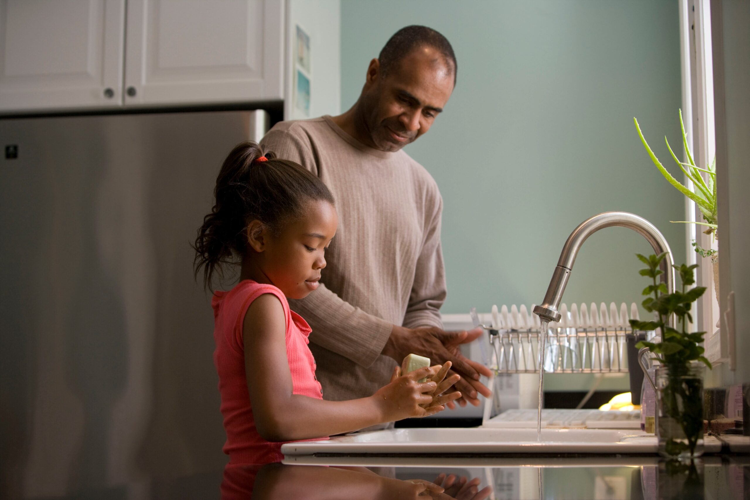 Image of a male adult washing his hands at a sink with a child