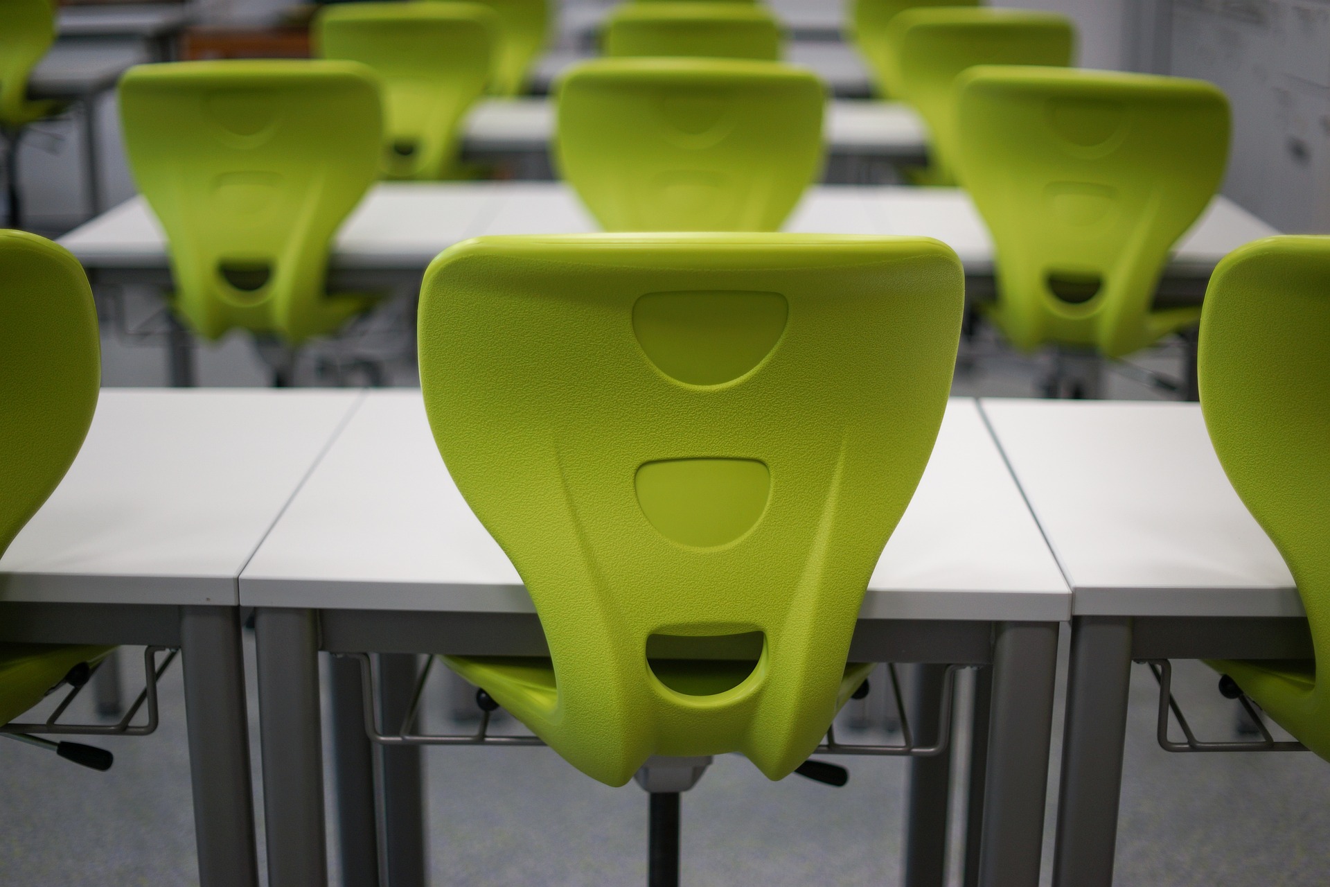 Close up shot of green office chairs around rows of desks