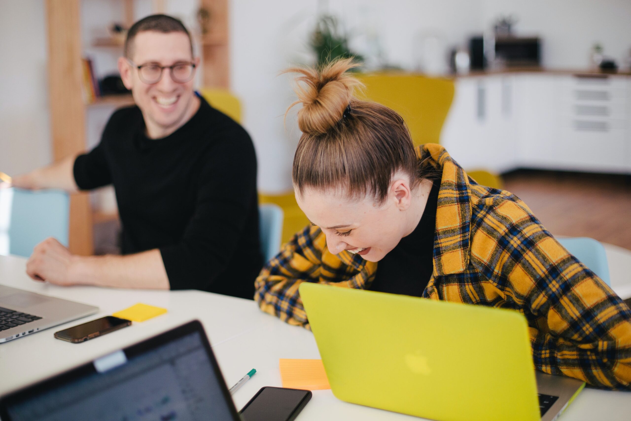 Image of a male and female laughing whilst sat at a desk in front of laptops